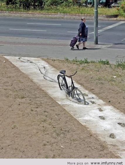 En person som går förbi en halvfärdig trottoar med en cykel inbäddad i cement.