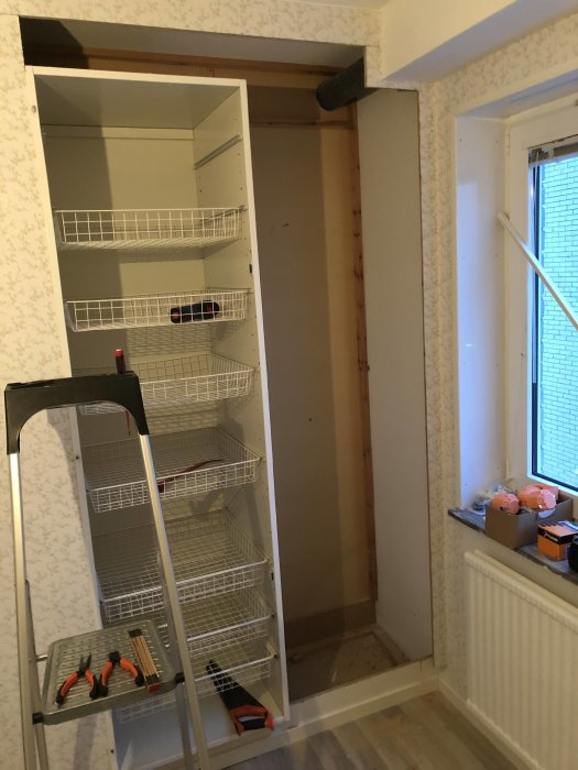 Renovering av garderob med öppen dörr och hyllor innanför, verktyg på stege och otillgängligt elutrymme.