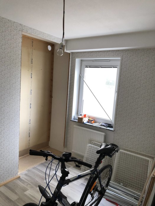 Ett rum under renovering med synliga kablar, outredd garderobsnisch och ett cykel framför.