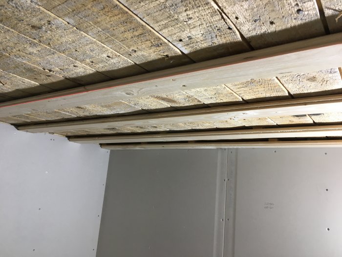 Ojämnt tak med masonitbitar och plank under konstruktion, synlig laserlinje, vägg av gipsskivor.