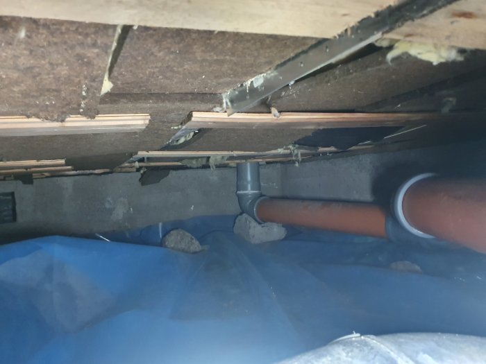 Krypgrund med installerad plast och synliga vattenansamlingar, rörledningar och isoleringsmaterial.
