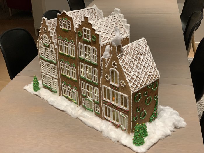 Handgjort pepparkakshus som föreställer ett julpyntat kvarter med snödekor på bord.