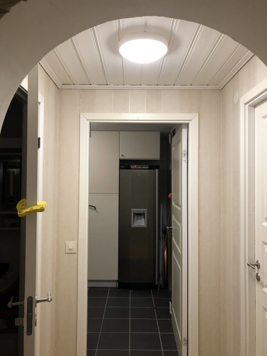 Nyinstallerad taklampa i en hemkorridor med vit bågformad dörrkarm och svarta golvplattor.