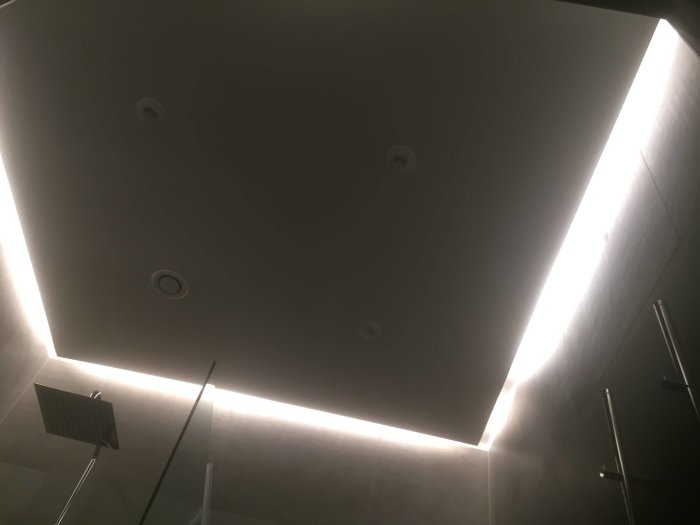 Modern badrumstak med infällda spotlights och LED-belysning längs väggkanten.