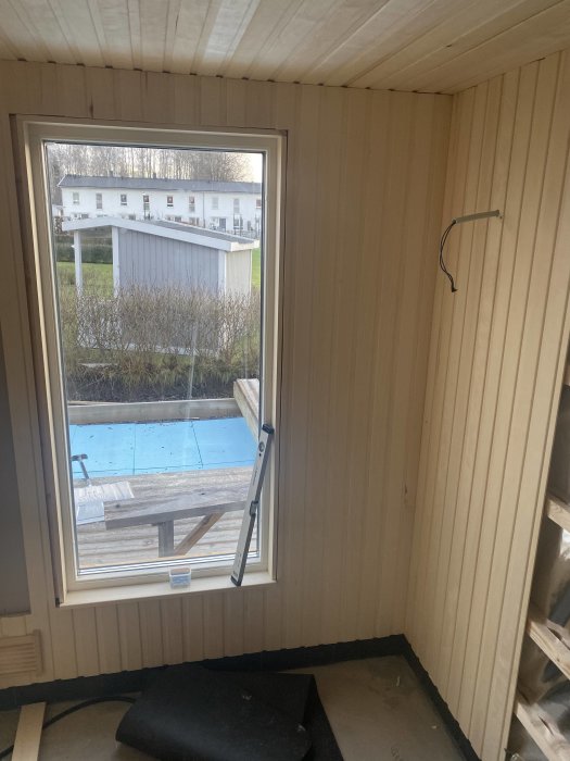 Inre hörn av en bastu under konstruktion med träpanel och ett fönster, samt en första installerad ventilationsöppning.