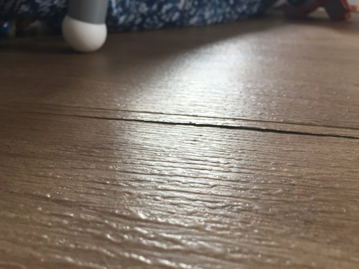 Närbild på ett sprucket laminatgolv med tydlig längsgående spricka mellan två brädor.