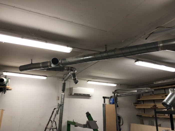 Delvis installerat spånsugssystem med aluminiumövergång och ventilationsrör i ett verkstadsrum.