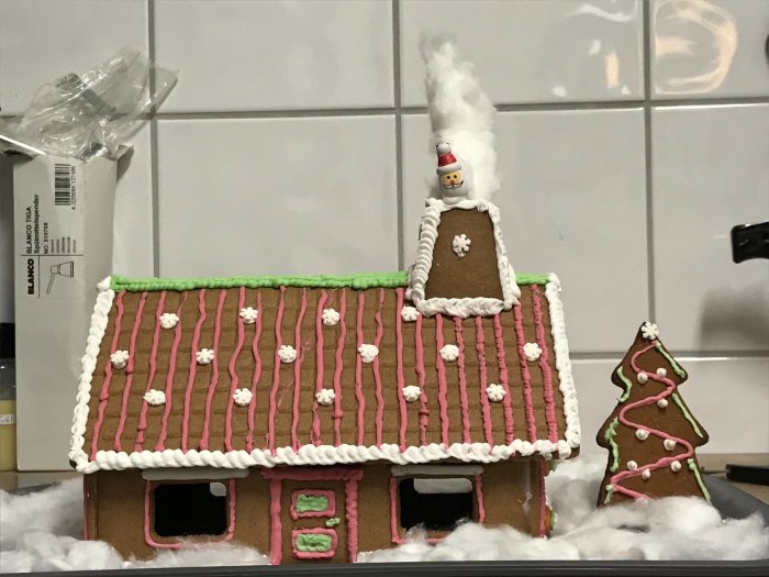 Hantverksmässig pepparkakshusmodell och hundkoja med dekorativt sockerglasyr.