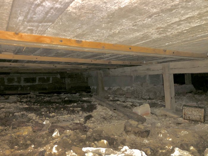 Underbelyst bild av krypgrund med tvivelaktig träbjälke och stolpar som inte verkar säkert förankrade.