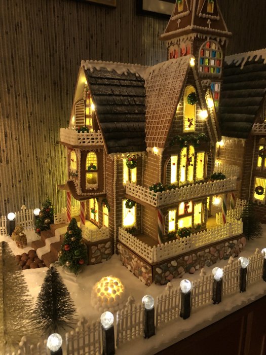 Elaborate edible gingerbread house with lit-up fence, LED under-roof lighting, and snow lanterns, with a brick facade design.