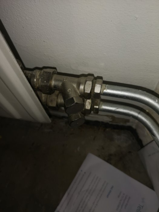 Närbild på en radiatorventil och anslutande rör inför gipsning bakom element i en lägenhetsrenovering.