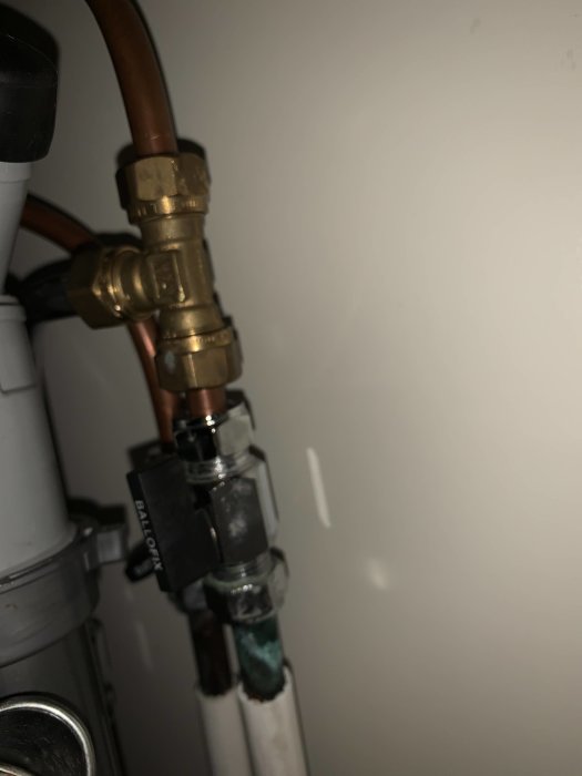 Närbild på ärgiga ballofixventiler och rörkopplingar under ett köksskåp, fuktmärken synliga.