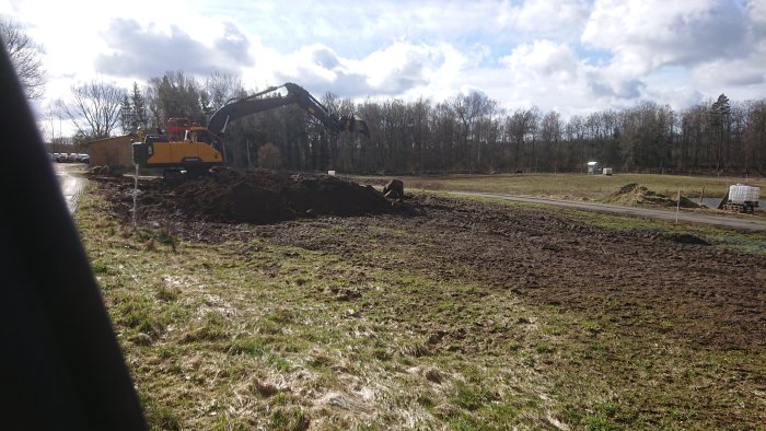 Grävmaskin som tar bort jord för att anlägga en paddock, med skog och öppen himmel i bakgrunden.