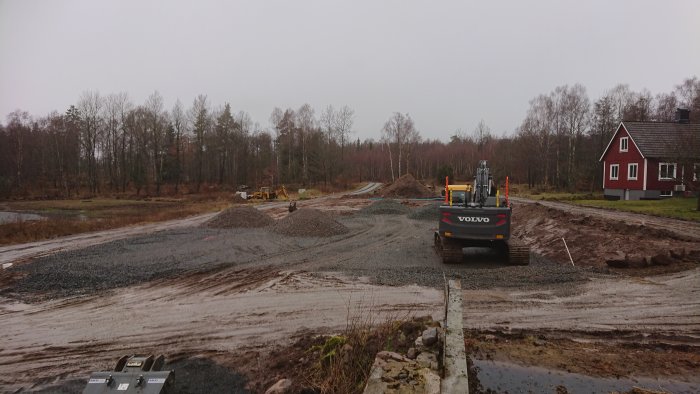 Byggarbetsplats med grävmaskin och högar av makadam i en process på att skapa en paddock.