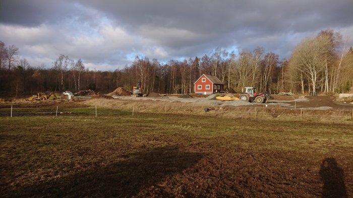 Byggarbetsplats med grävmaskiner och traktor för anläggning av paddock, med hus i bakgrunden.