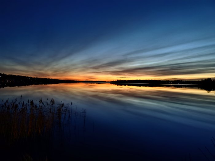 Solnedgång med dramatiska färger och reflektioner över en stilla sjö i Osby.