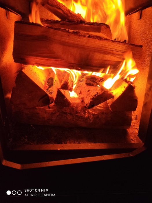 Eldstad med flammande ved som brinner, något sot på glasets nederkant.