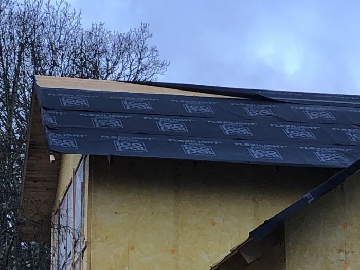 Tak under konstruktion med underlagspapp på gult hus, ogynnsamt väder för byggprojekt.