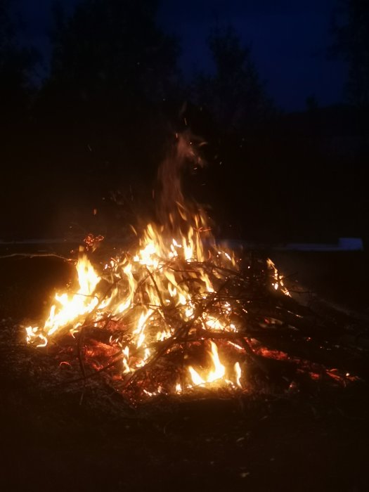 En eldig brasa utomhus i mörkret med flammande träbitar och gnistor.