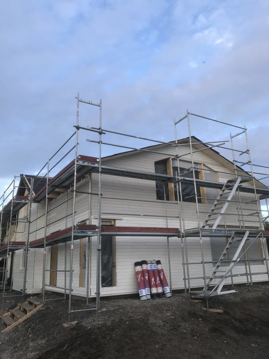 Hus under utbyggnad med byggnadsställningar runtomkring och material på marken.