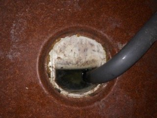 Gammal golvbrunn med en lös klämmring och skruvhål, i behov av tillfällig reparation.