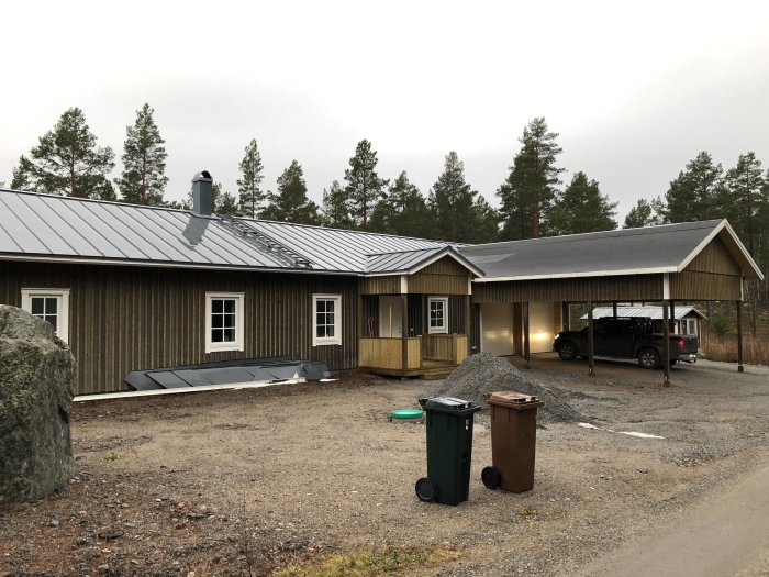 Nybyggt lösvirkeshus med vidbyggt dubbelgarage och carport, omgivet av skogsmark.