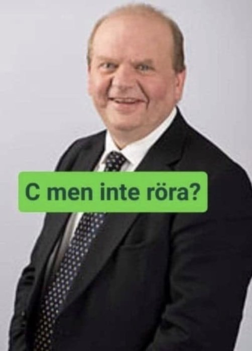 Man i kostym med textremsa framför sig: "C men inte röra?