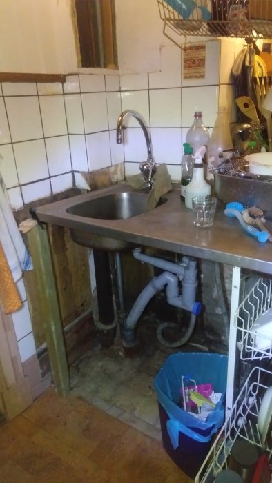 Gammalt kök i behov av renovering med synlig rörledning och slitet trägolv.