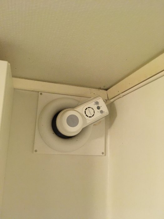 Ventilationsfläkt monterad i hörnet av ett tak i ett badrum, med reglage för inställningar.