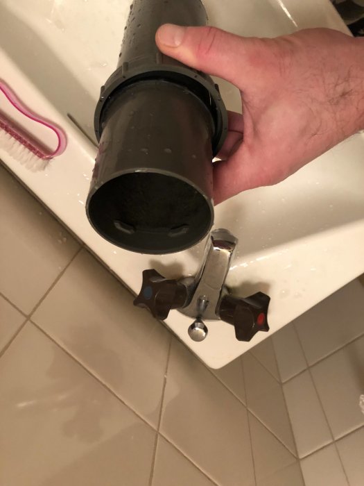 Hand som håller ett 65mm avloppsrör nära en rostfri vask med kranar.