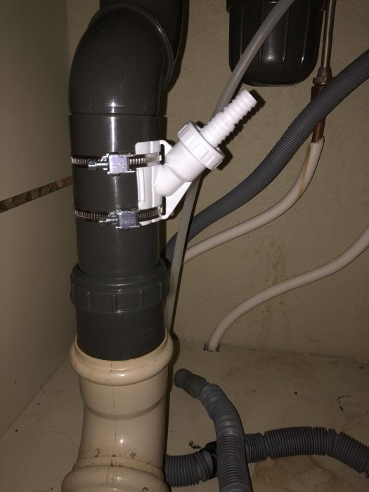 Installation av avloppsrör med slangklämmor och vit anslutning för slangen.