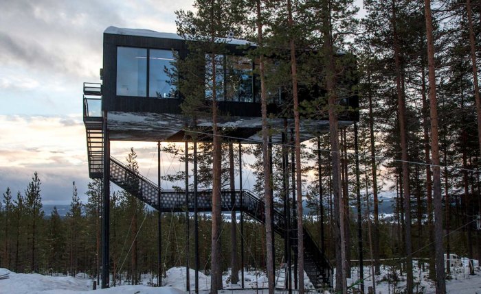 Modernt trädhus med stora fönster beläget i ett snötäckt skogslandskap i Swedish Lapland.