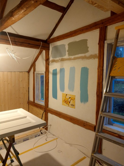 Ommöblerat sovrum med träreglar, spånskiva, provmålade färgprover och en panelvägg.