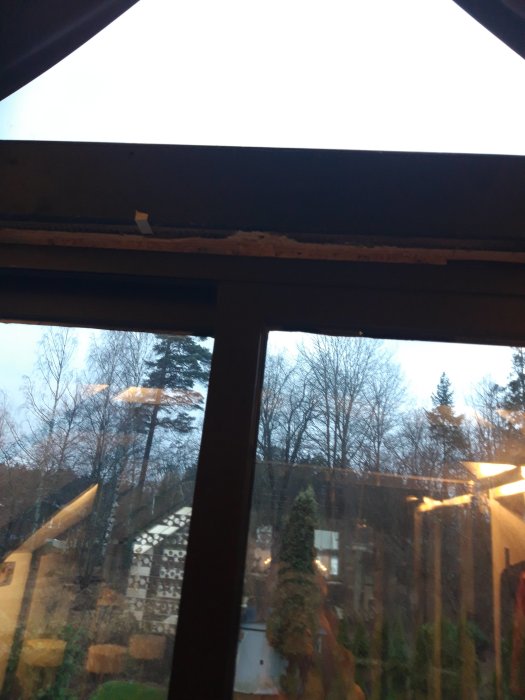 Utsikt genom ett fönster i ett vindsrum med synliga takbjälkar och träd utanför.