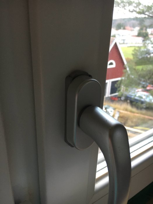 Barnlås monterat på ett fönsterhandtag med utsikt över bostadsområde i bakgrunden.