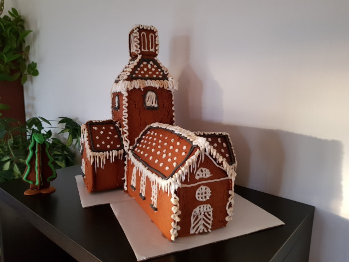 Pepparkakskopia av en kyrka med vita dekorationer på bord mot växtbakgrund.