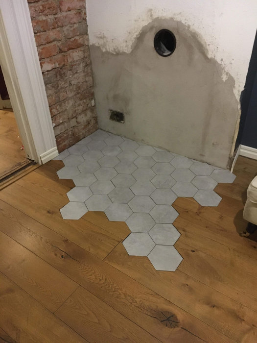 Nyplattlagd hexagonal kakel framför en ofärdig vägg och tegelsten där en kamin ska installeras.