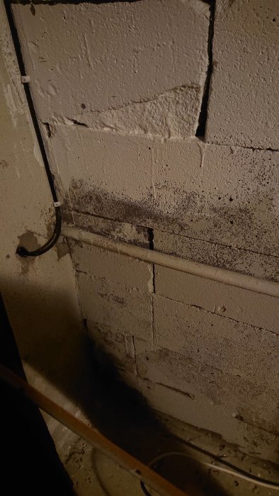 Elrör som kommer ut från ett hål i en betongvägg och löper horisontellt längs väggen med tecken på ombyggnad.