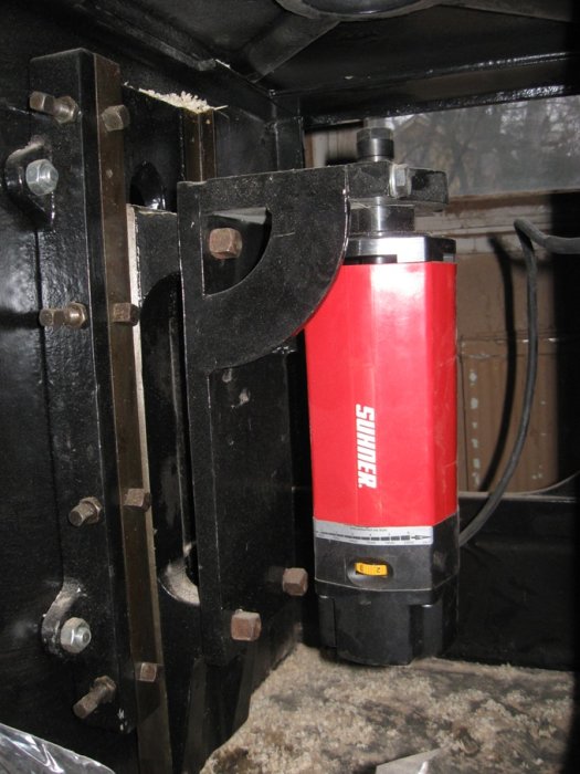 En installerad röd och svart hydraulisk stötdämpare monterad mellan stålstag.
