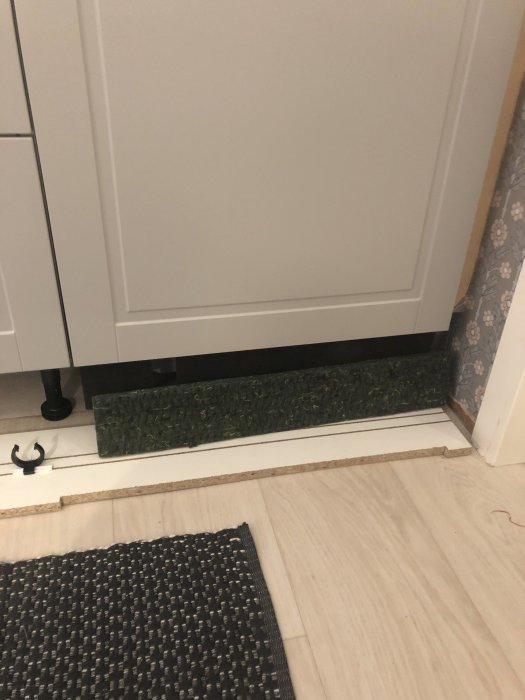 Ljudisoleringbit framför diskmaskinslucka på köksgolv, undrar om placering under luckan.