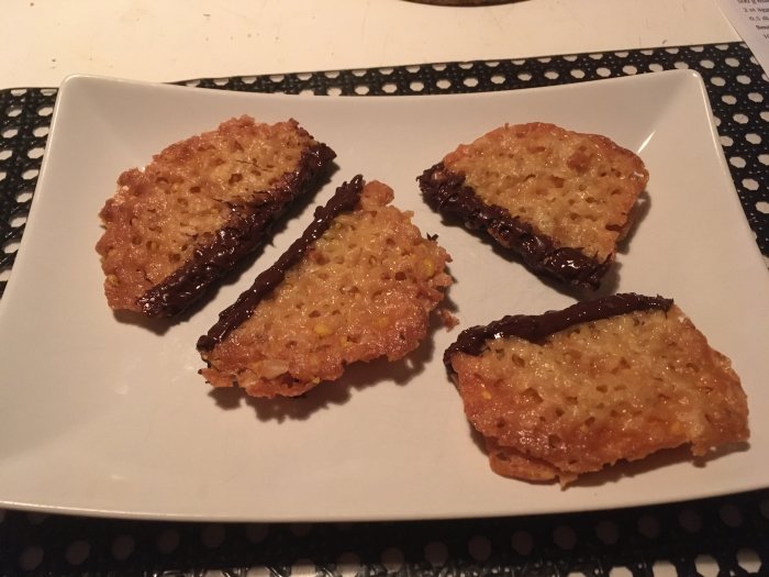 Hembakade knäckeflarn halvt doppade i mörk choklad på vit tallrik.
