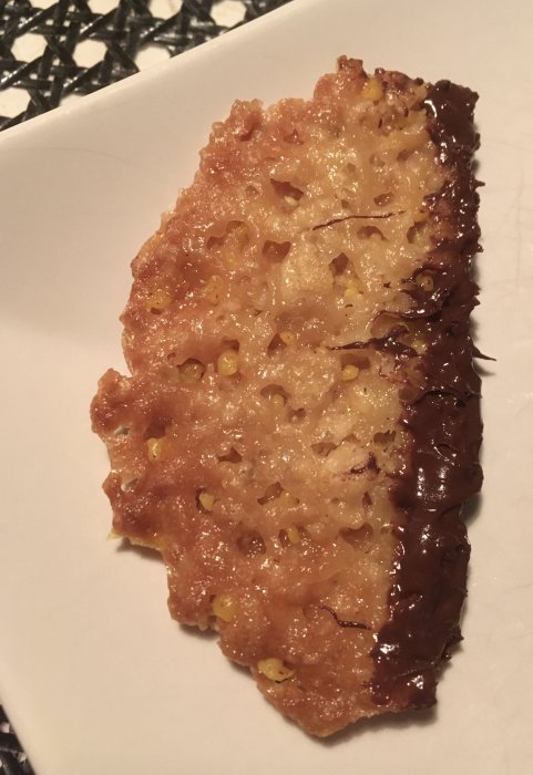 Hembakt knäckeflarn med gyllene havregryn och kant doppad i mörk choklad på vit tallrik.