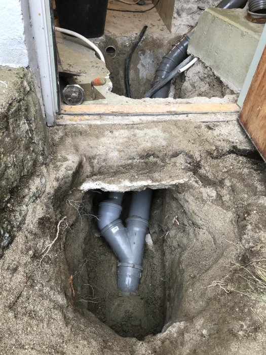 Grävd hålighet vid byggnadsfundament med nyinstallerade avloppsrör.