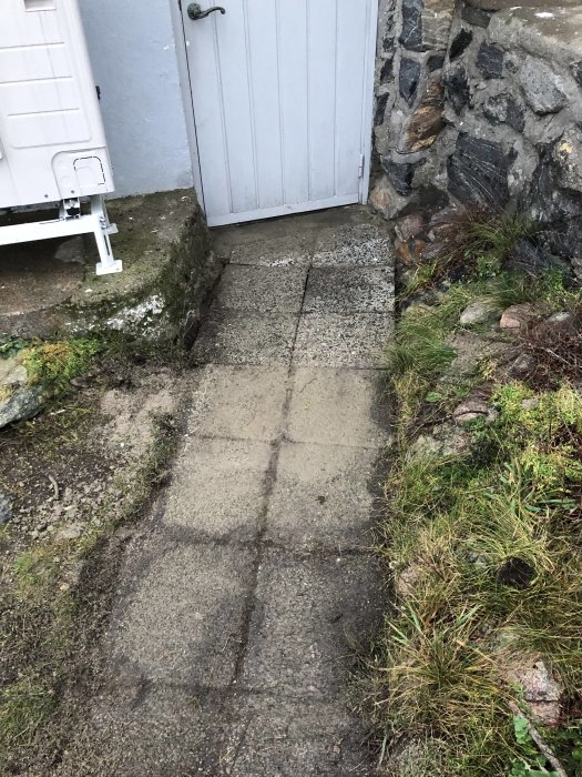 Nylagade betongplattor på en trädgårdsgång framför en blå dörr med stenmur.