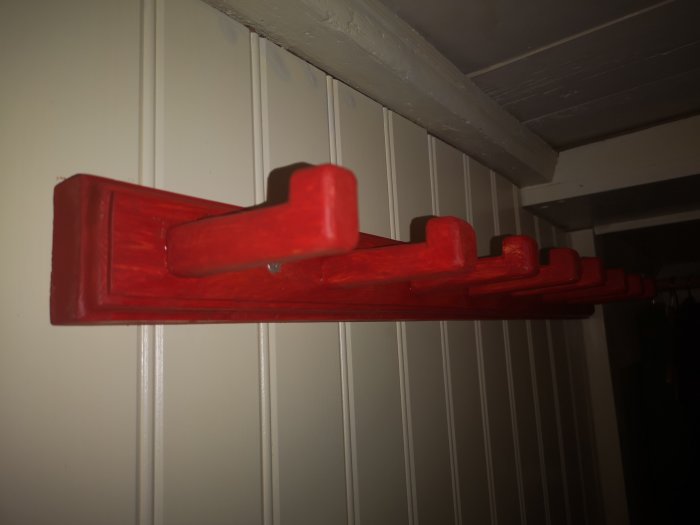 Rödmålad, täljd träbräda med profilering, monterad på vägg, behandlad med linoljelasyr.