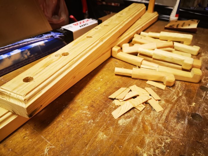 Täljda träbrädor och delar på en verkstadsbänk, förberedda för montering med linoljelasyr i engelsk röd.