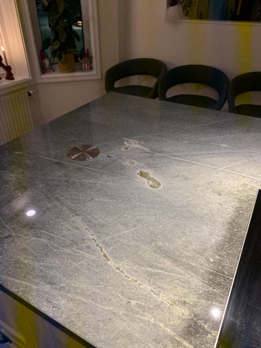 Kvartsitbänkskiva med mörka fläckar och oljade ytor som reflekterar rummets belysning.