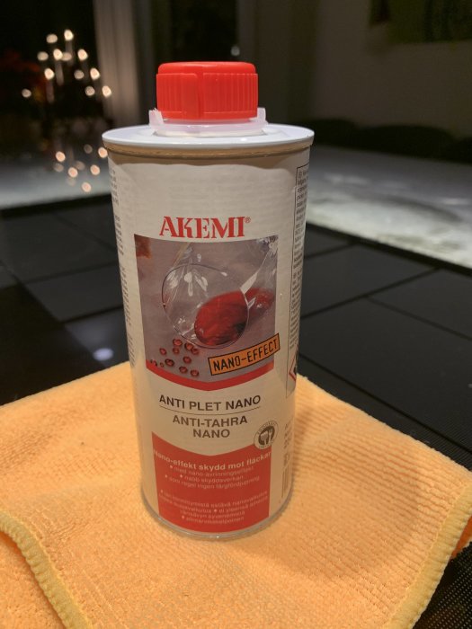 Flaska med AKEMI Anti-Plet Nano olja på en orange trasa med mörk kvartsitbänkskiva i bakgrunden.