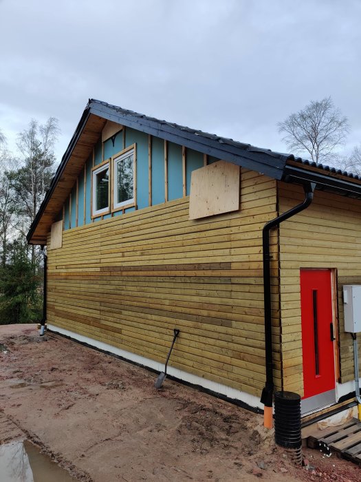 Hus under renovering med nyinstallerade stuprör och nylagd dränering, samt tillfällig träskydd på väggen.