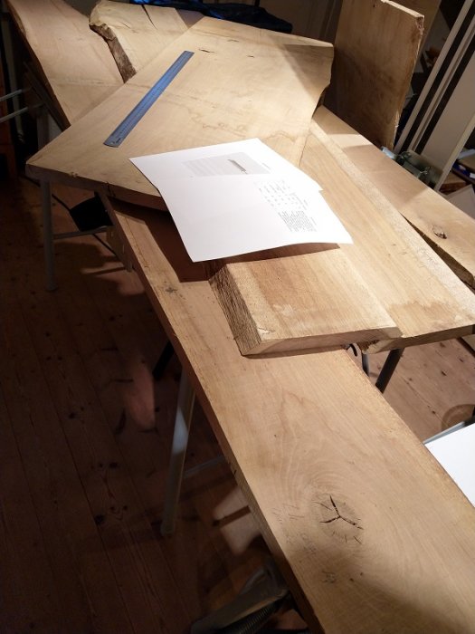 Obehandlade träplankor och en ritning på ett bord utgör grunden för ett möbelsnickeri-projekt.